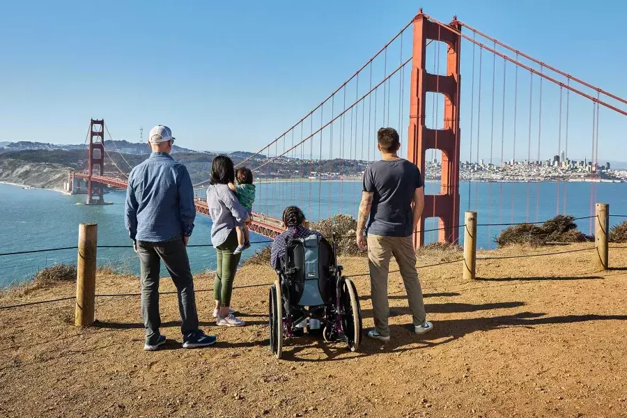 Un gruppo di persone, 包括一个坐轮椅的人, 从后面可以看到他从马林海德兰看金门大桥.