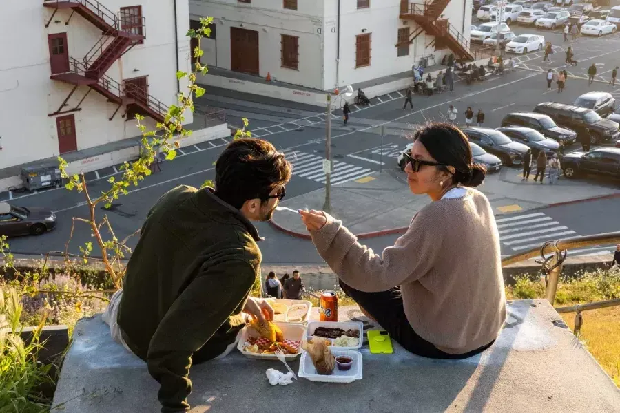 A couple dines al fresco at Fort Mason Center 在贝博体彩app. The woman feeds her companion a taste of food.