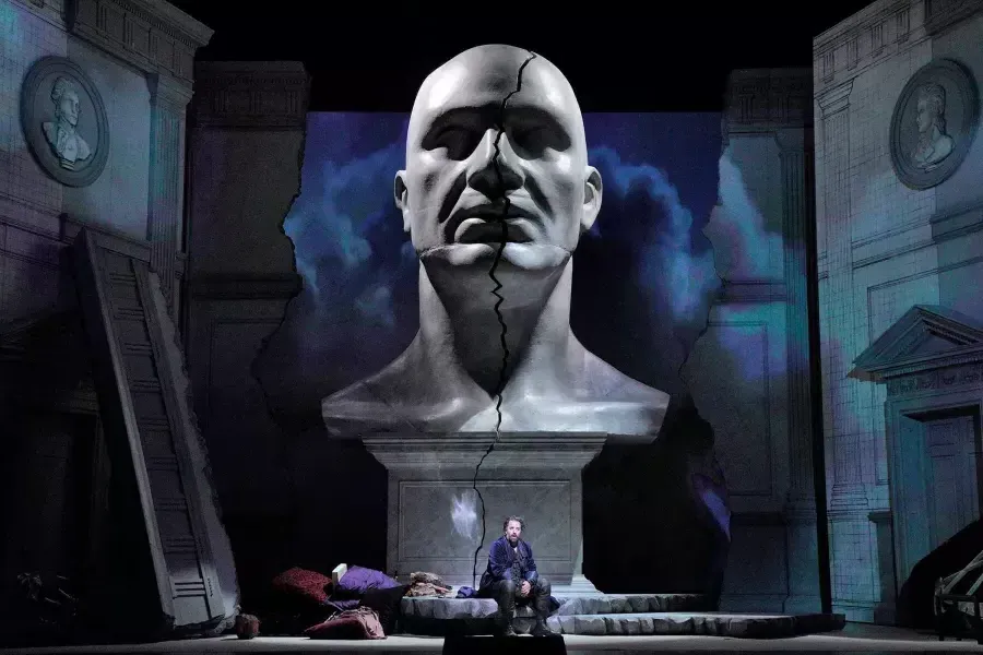 A giant bust of a man looms over two actors on stage in a production of Don Giovanni in San Francisco.