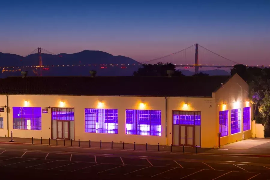梅森堡的建筑在晚上被紫色的室内灯照亮, with the bridge in the background.