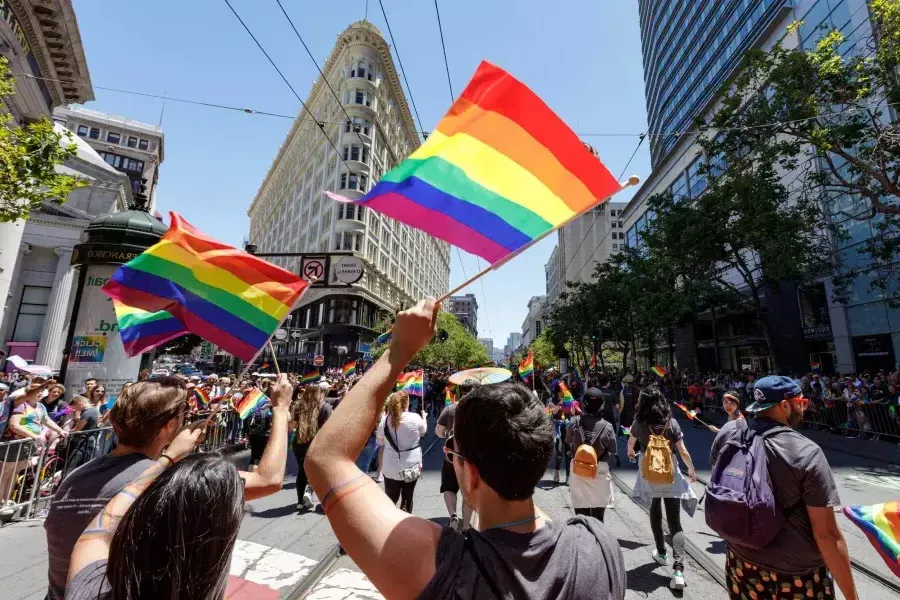 人民walking in the San Francisco Pride parade wave rainbow flags.