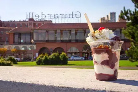 A chocolate sundae sits in the foreground with 吉尔德利 Square in the background.