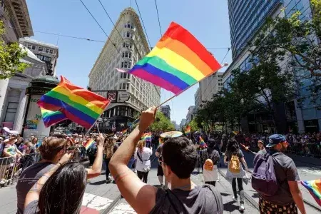 People walking in the San Francisco 骄傲 parade wave rainbow flags.